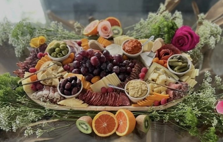 Grazing board styled with sliced oranges, kiwi, olives and greenery across the front