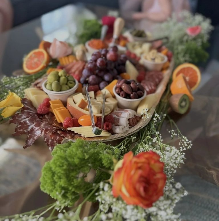 Charcuterie board surrounded by roses and baby's breath with grapes, olives and cured meats