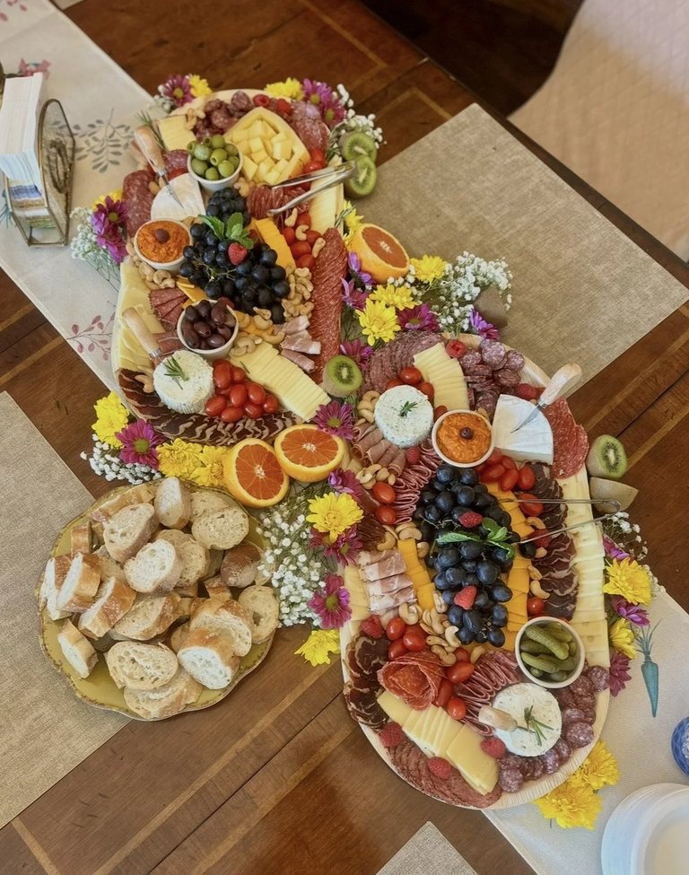 Two large charcuterie boards styled along a linen table runner with a platter of sliced baguette