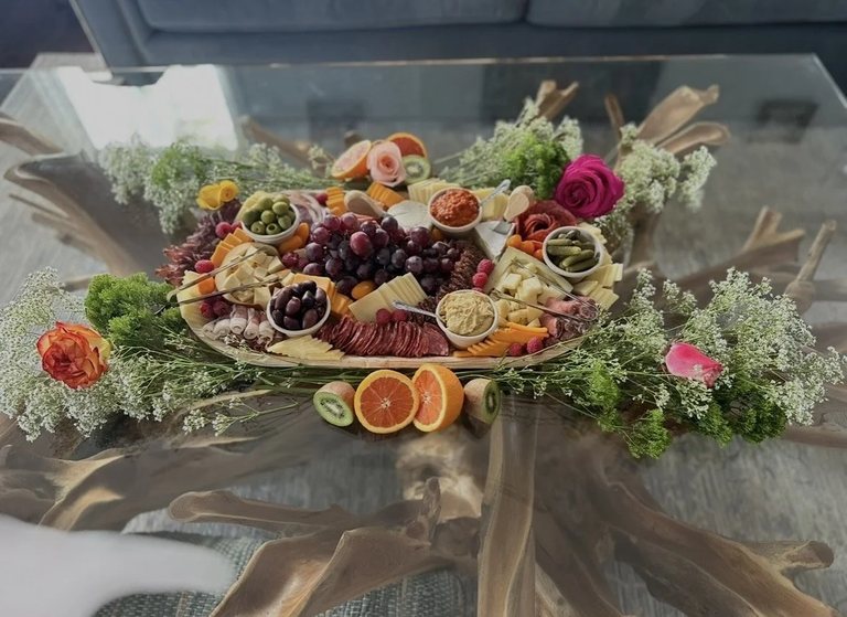 Oval grazing board on a glass driftwood table framed with greenery, roses and citrus