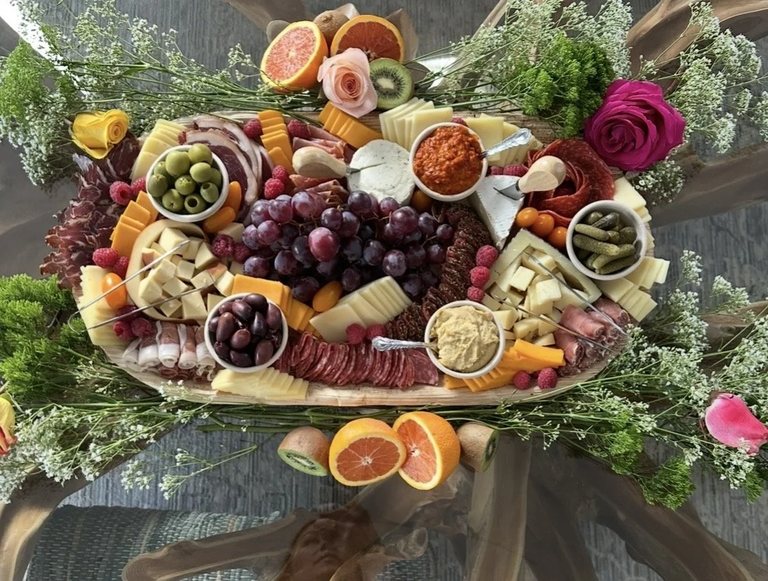 Overhead view of a grazing board with grapes, cheese wedges, cured meats, dips and blood orange