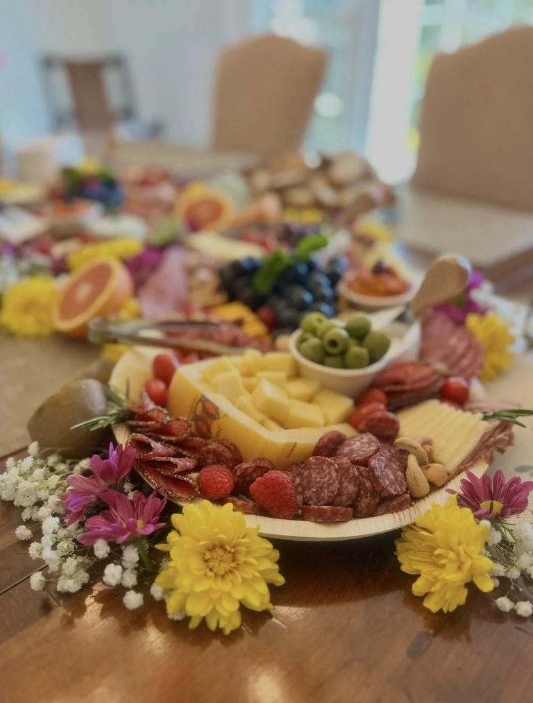 Close-up of salami, aged cheese, raspberries and cashews framed by yellow and pink blooms